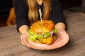 Cropped photo of woman sitting at table, holding plate with fresh burger with lettuce, onion, tomato, chicken. Cooking.