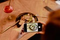 Cropped photo of woman sitting near salad and glass with red cocktail, holding smartphone, taking pictures of food. Royalty Free Stock Photo