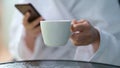 Cropped photo of a woman in a terry bathrobe holding mobile phone and cup