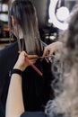 Cropped photo of woman hairstylist making hairstyle cutting tips of long dark hair, holding scissors, pink barber comb. Royalty Free Stock Photo