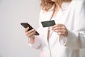 Cropped photo, young female in white suit holds phone and credit card in her hands isolated over grey background Royalty Free Stock Photo