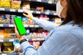 Cropped photo of a young woman with face mask using mobile phone and buying groceries in the supermarket during virus Royalty Free Stock Photo