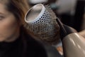 Cropped photo of young woman sitting in beauty salon. Beautician making hairstyle using dryer, brush, creating curls.