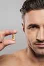 Cropped picture of of mature man holding pill. Looking camera.