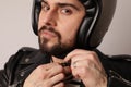 Cropped portrait of bearded biker in leather jacket fasten a motorcycle helmet. Royalty Free Stock Photo