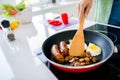 Cropped portrait of chef woman hand hold wooden spatula electric stove frying pan sausage mushroom egg homemade Royalty Free Stock Photo