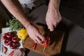 Cropped portrait of male hands cutting yellow bell pepper in the kitchen with knife on wooden cutting board. Onion, pumpkin, hot