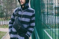 Cropped portrait of young bearded man in striped hoodie with black leather crossbody bag. Street wear, fashion city accessories Royalty Free Stock Photo