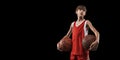 Cropped portrait of young boy, basketball player in red uniform standing, posing with ball isolated over black Royalty Free Stock Photo