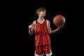 Cropped portrait of young boy, basketball player in red uniform standing, posing with ball isolated over black Royalty Free Stock Photo