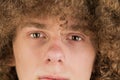 Cropped portrait of a young curly European man with long curly hair and a defiant gaze looks into the frame close-up. very lush