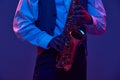 Cropped portrait of young man, saxophonist, musician in shirt and vest holds wind instrument against studio background Royalty Free Stock Photo