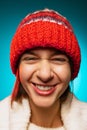 Cropped portrait of young merry, laughing girl in red winter hat smiling at camera isolated over blue background Royalty Free Stock Photo