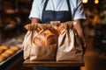 Cropped shot of bakery owner or employee holding freshly baked wheat bread loaves packed in craft paper bags. High Royalty Free Stock Photo