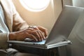 Cropped shot of businessman in suit typing, working on laptop while sitting in airplane cabin