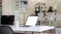 Cropped shot of workplace with blank screen tablet, laptop, office supplies and coffee cup on white table with blurred office room Royalty Free Stock Photo