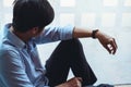 Cropped shot of depressed man sitting on the floor by window at office walkway feeling unhappy. Depression and anxiety disorder