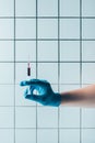 cropped shot of doctor in glove holding syringe of blood in front of tiled