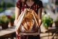 Cropped shot of female bakery owner or employee holding freshly baked wheat bread loaf packed in a craft paper bag. High Royalty Free Stock Photo