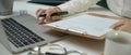 Female doctor writing medical certificate on laptop while looking information on patient chart Royalty Free Stock Photo