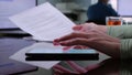 Cropped shot of female hand holding document and scrolling smartphone sitting at desk in office