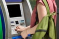 Cropped shot of female teenager carries green bag, wants to withdraw cash, stands near ATM machine, enters pin, makes payment. Sec Royalty Free Stock Photo