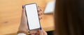 Cropped shot of female using mock-up smartphone on wooden desk Royalty Free Stock Photo