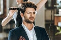 Cropped shot of hairstylist combing and drying hair to handsome young man