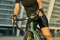 Cropped shot of hands of female cyclist in black cycling garment and protective gear riding bike in city, training