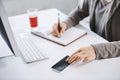 Cropped shot of hands writing down in note pad and touching smartphone. Employee working in office, checking mail via