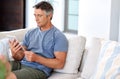 Staying up to date with technology. Cropped shot of a handsome mature man sitting on his living room sofa and using a Royalty Free Stock Photo