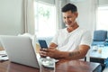 Feeling productive at home. Cropped shot of a handsome young man using his cellphone while working on a laptop in the