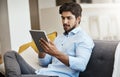 Doing a little surfing on the net. Cropped shot of a handsome young man using his tablet while sitting on his sofa in