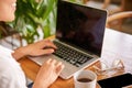 Cropped shot of laptop screen and female hands typing, cafe interior and cup of coffee with glasses on table Royalty Free Stock Photo