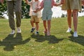 Cropped shot of legs of happy young family with two little kids holding hands, walking together in green summer park Royalty Free Stock Photo