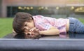 Cropped shot of lonely little boy lying on bence in the park, Kid with bored face using his fingers writing something, Sad child Royalty Free Stock Photo