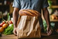 Cropped shot of male bakery owner or employee holding freshly baked wheat bread loaf packed in a craft paper bag. High Royalty Free Stock Photo