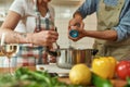 Cropped shot of man adding pepper, spice to the soup while woman stirring it with a spoon. Couple preparing a meal