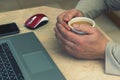 Cropped shot of a man`s hands holding a cup of coffee typing on a laptop that is on a wooden desk. Busy man working at home. male Royalty Free Stock Photo