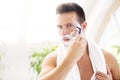 Handsome man shaving his beard while standing in front of a mirror Royalty Free Stock Photo