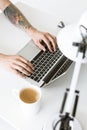 Cropped shot of man typing on laptop placed at white tabletop with cup of coffee