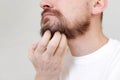 Cropped shot mans hand is unrestrained scratching unshaven chin. Overgrown unkempt male in white t shirt with thick