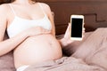 Cropped shot of pregnant woman showing smartphone with black screen in bed Royalty Free Stock Photo