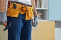 Cropped shot of professional repairman wearing a tool belt, holding a hammer and an adjustable wrench in his hands while Royalty Free Stock Photo