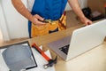 Cropped shot of repairman worker in uniform wearing tool belt, holding utitlity knife and using laptop while standing Royalty Free Stock Photo