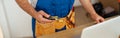 Cropped shot of repairman worker in uniform wearing tool belt, holding utitlity knife and using laptop while standing Royalty Free Stock Photo