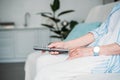 cropped shot of senior woman with remote control watching tv on sofa at home