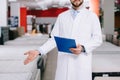 cropped shot of shop assistant with notepad pointing at orthopedic mattresses in white coat