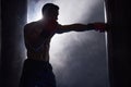 Working on his technique. Cropped shot of a silhouetted young male boxer working out on a punching bag in the gym. Royalty Free Stock Photo