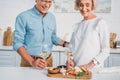cropped shot of smiling senior couple holding glasses of wine and looking at delicious snacks Royalty Free Stock Photo